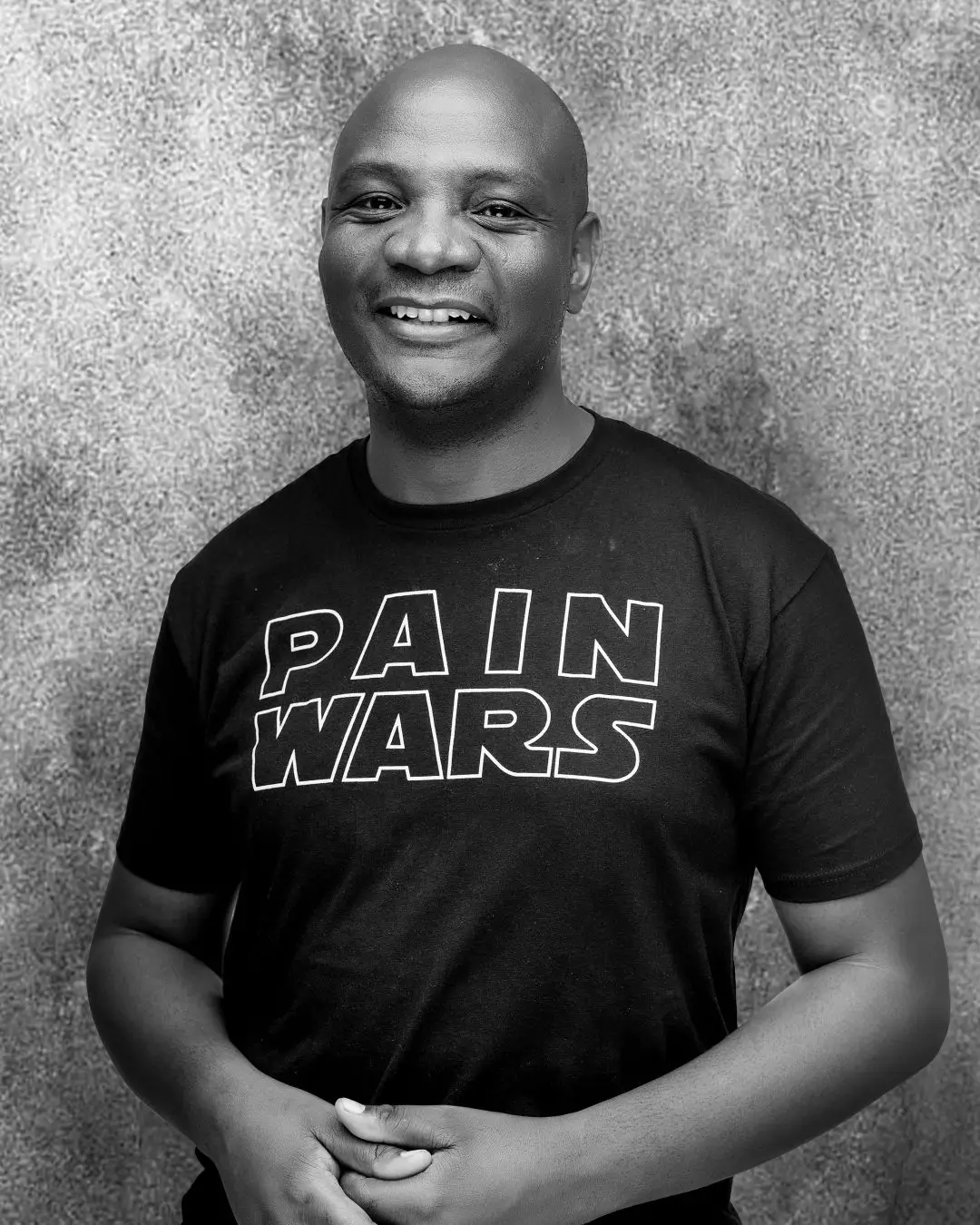 Simon Mambariza, smiling, in a black T-shirt against a textured grey wall